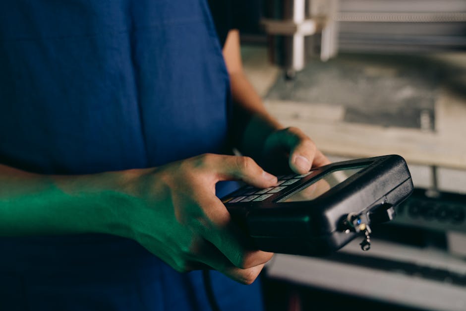 Close-up of technician using a handheld control device in a manufacturing setting.