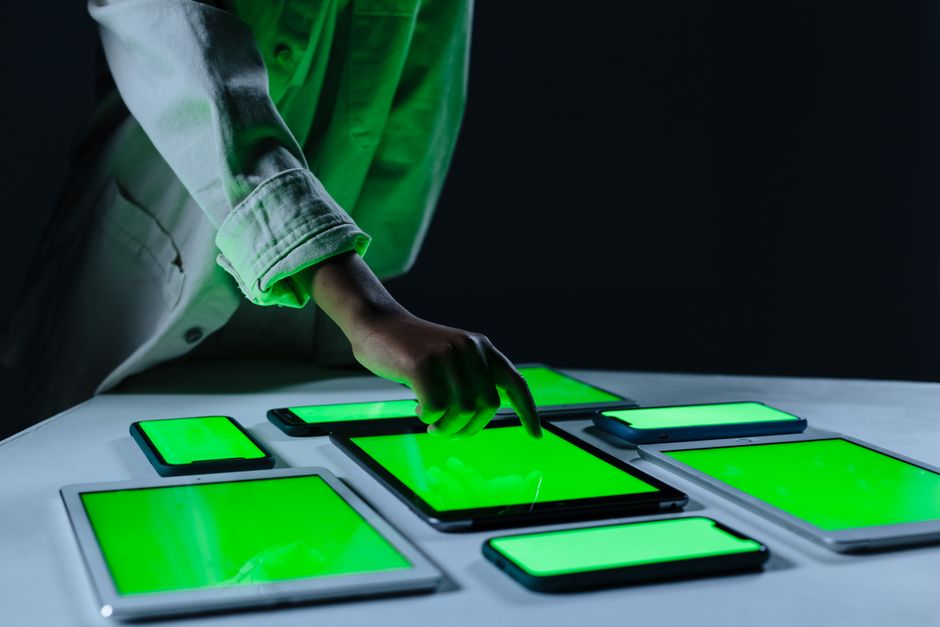 Hand interacting with multiple digital tablets on a green screen setup indoors.